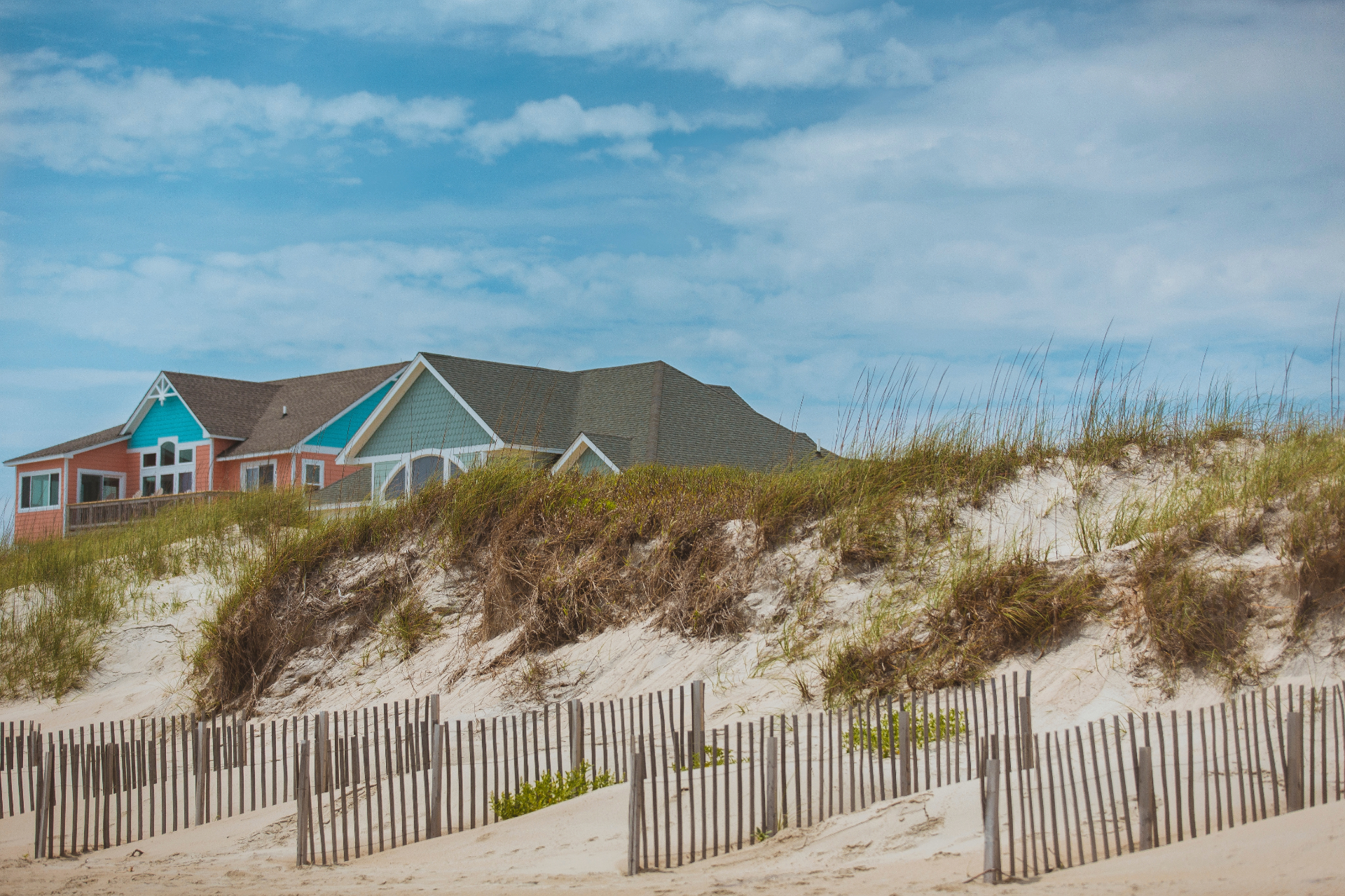 Big bright colorful oceanfront beach houses Outer Banks, North Carolina. Sand dunes, beach grass and wooden fence in the foreground, and clear blue sky